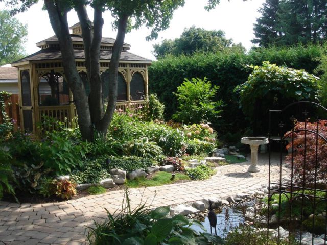 wooden 10 by 16 foot oval gazebo surrounded by lush gardens